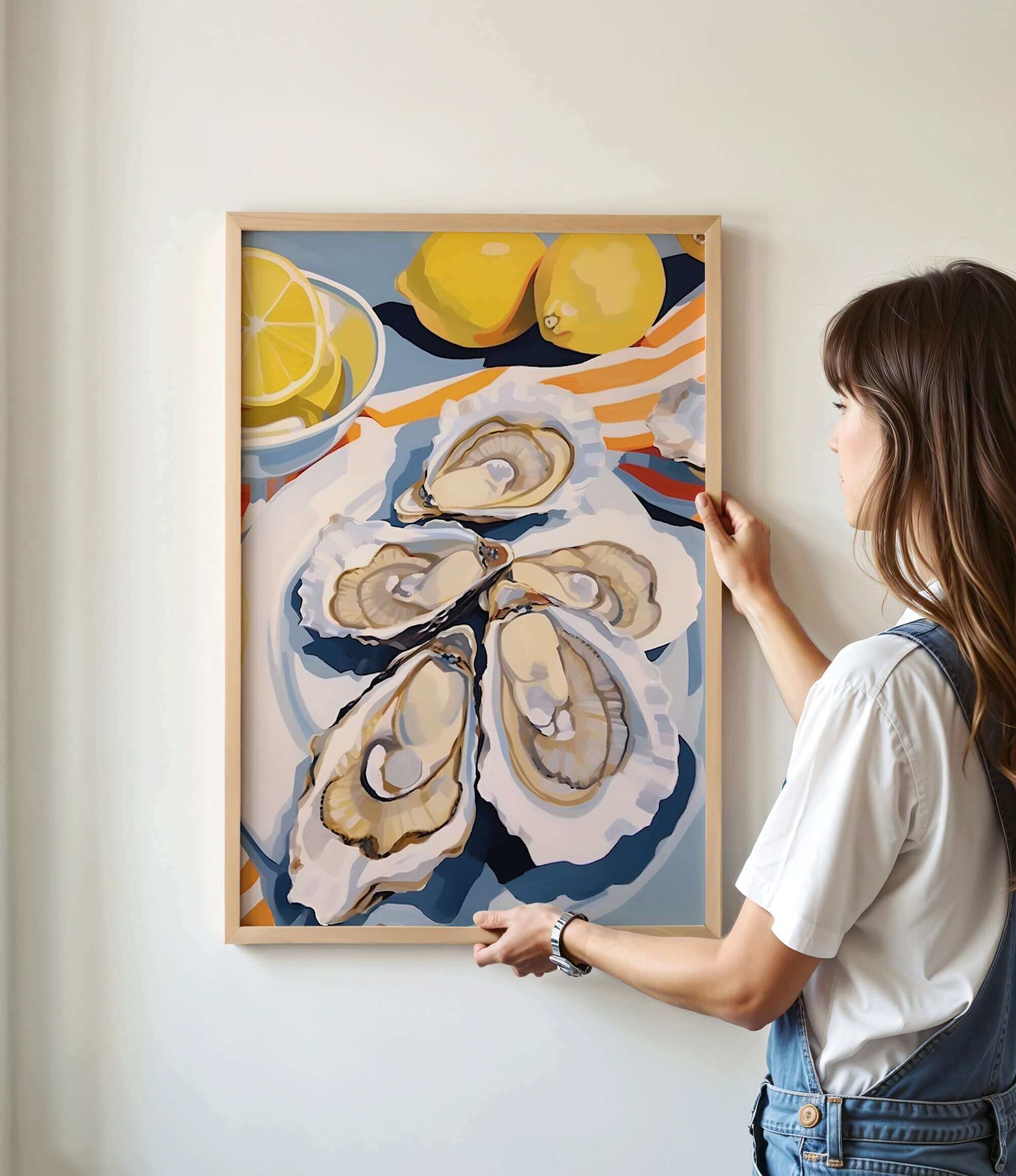 A woman is hanging a framed artwork on a wall, which features a vibrant painting of oysters and lemons.