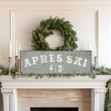 a fireplace mantel decorated with a wreath, candles, and a sign that reads "APRÈS SKI".