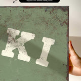 a hand holding a piece of artwork with a distressed, green background and a large white letter "K" prominently displayed.