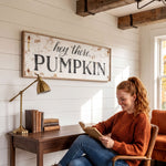 A woman is sitting at a desk, reading a book, with a lamp and a stack of books nearby. Above her, there is a sign that says "hey there, PUMPKIN".