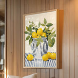 A framed painting of a vase filled with lemons and green leaves is hanging on a wooden wall.