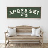 a wooden bench with two pillows, and above it is a green sign with white text that says "APRÈS SKI".
