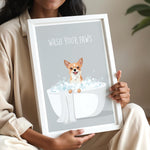 A woman is holding a framed poster with an illustration of a dog sitting in a bathtub filled with bubbles, accompanied by the text "WASH YOUR PAWS".