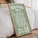 The Beach House Rules Sign, Painted Wood, Seagrass, with white text, leans against a bed in a sunlit bedroom, bringing cozy coastal charm and stylish wall art to the space.