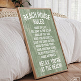 The Beach House Rules Sign, Painted Wood, Seagrass, with white text, leans against a bed in a sunlit bedroom, bringing cozy coastal charm and stylish wall art to the space.