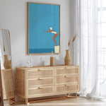 a modern, minimalist bedroom with a large mirror, a wooden dresser, and a framed artwork depicting a woman in a swimming pose.