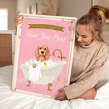 A woman is sitting on a bed holding a framed poster with a cocker spaniel dog in a bathtub.