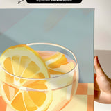 a close-up of a glass containing a slice of orange, with a hand holding the canvas.