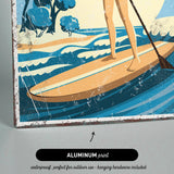 A woman is standing on a surfboard and paddling through the waves, with a beach and trees in the background.