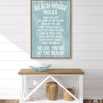 A Beach House Rules Sign in painted wood, in the Tide color, hangs above a wooden console table with decorative items and baskets, creating charming beach house wall decor.