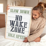 a woman sitting on a bed holding a sign that says slow down no wake zone