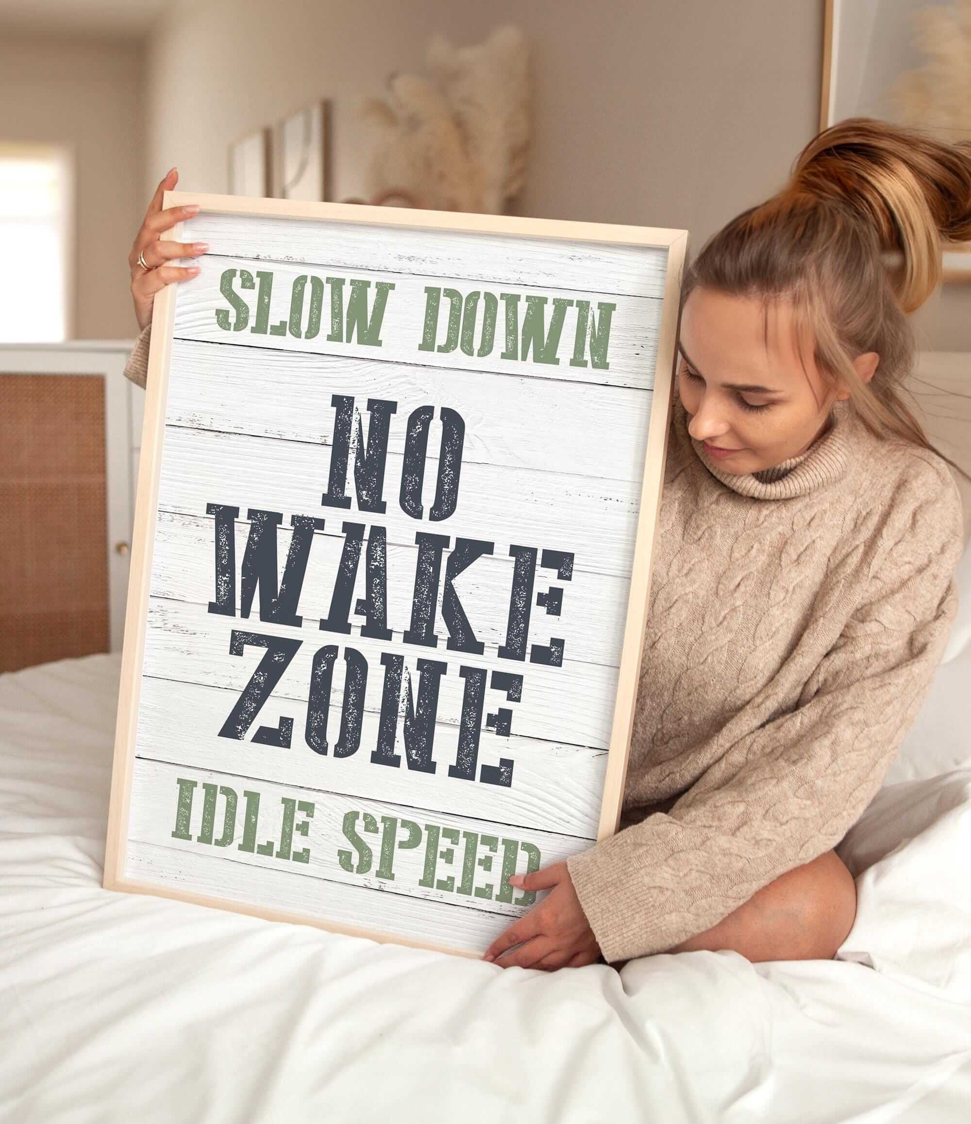 a woman sitting on a bed holding a sign that says slow down no wake zone