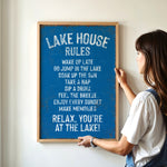A woman is hanging a blue sign on a wall that lists the "Lake House Rules" in white text.