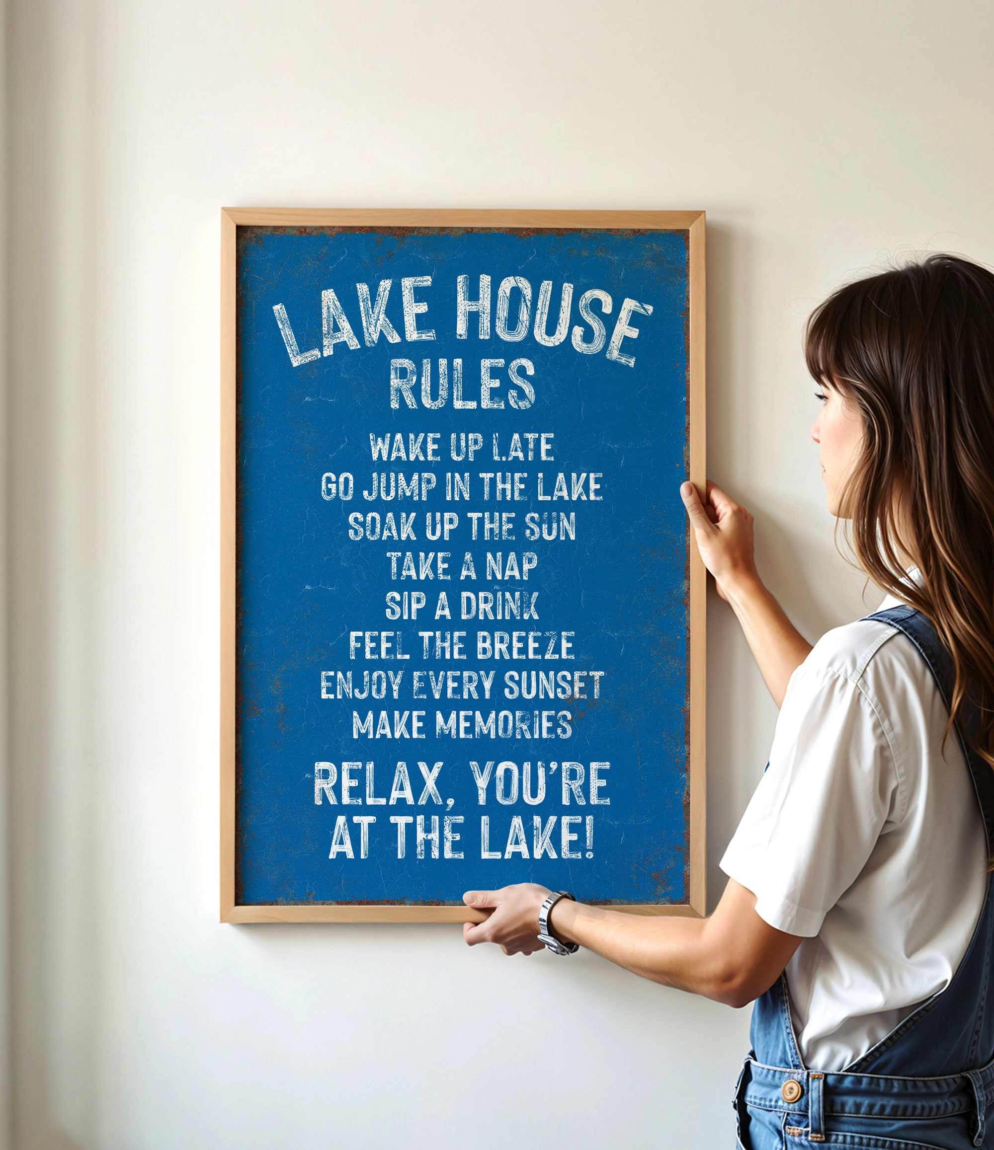A woman is hanging a blue sign on a wall that lists the "Lake House Rules" in white text.