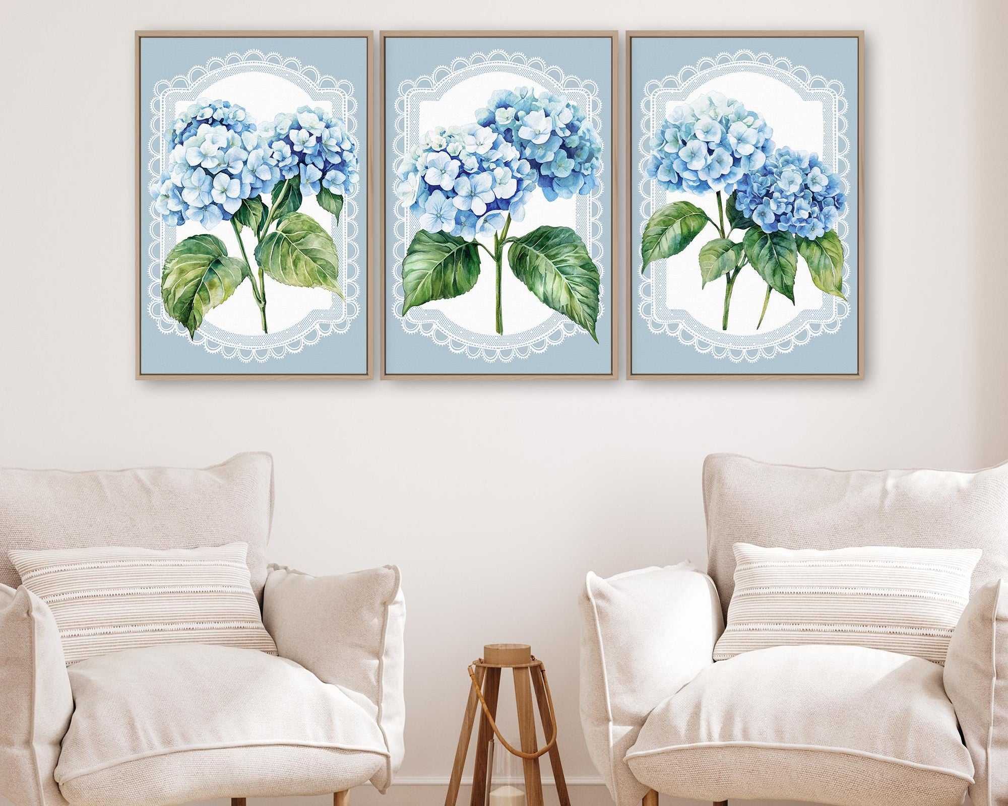 a living room with three framed paintings of blue hydrangeas hanging on the wall above two white armchairs.
