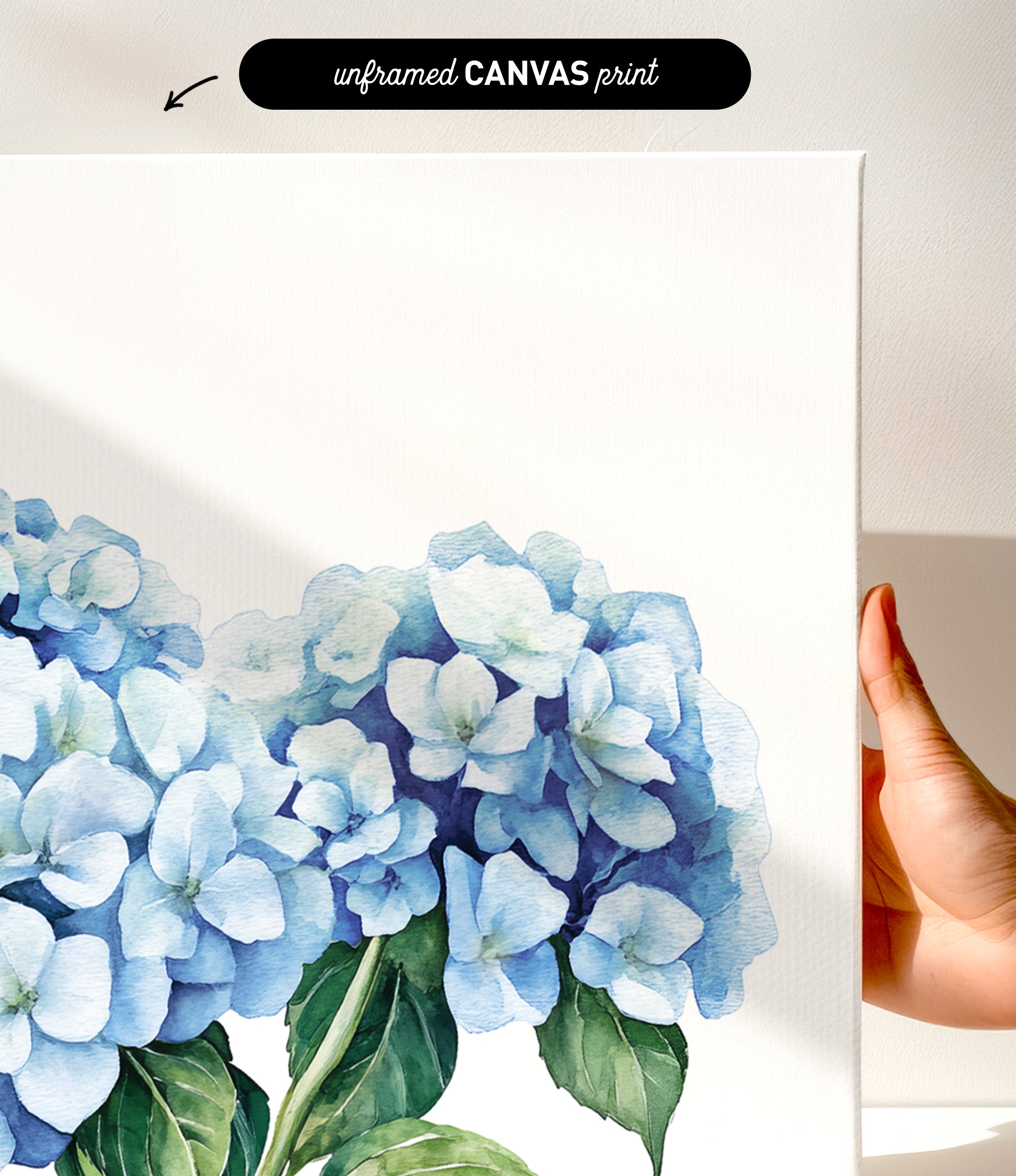 a hand holding a white canvas print of a watercolor painting of blue hydrangea flowers.