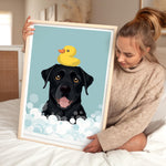 A woman is holding a framed picture of a black dog with a yellow rubber duck on its head, sitting on a bed.