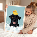 A woman is holding a framed picture of a black dog with a yellow rubber duck on its head, sitting on a bed.