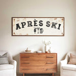 a rustic wooden dresser with a vintage-style sign hanging above it, which reads "APRÈS SKI". The dresser is situated between two white chairs, creating a cozy and inviting atmosphere.