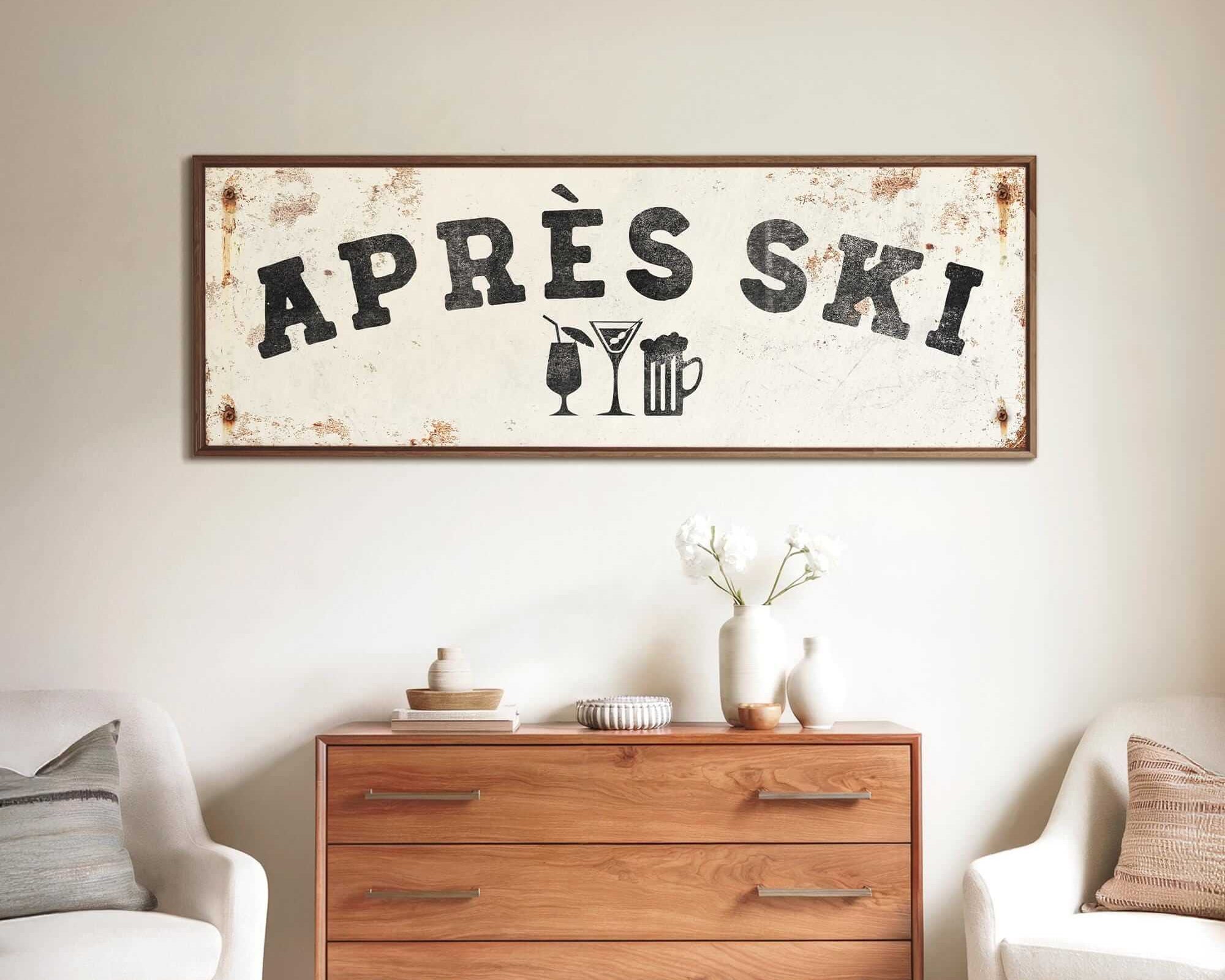 a rustic wooden dresser with a vintage-style sign hanging above it, which reads "APRÈS SKI". The dresser is situated between two white chairs, creating a cozy and inviting atmosphere.