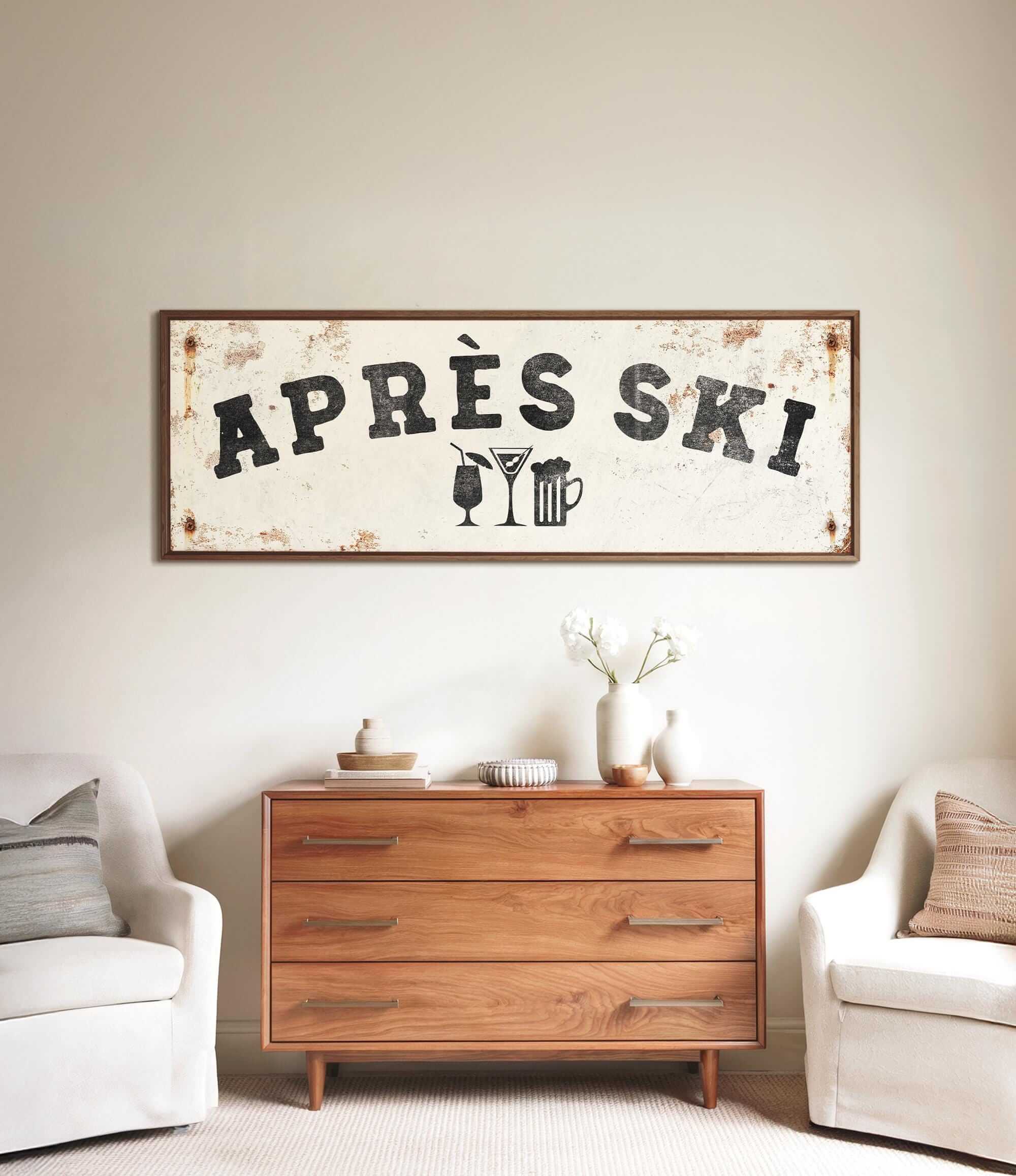 a rustic wooden dresser with a vintage-style sign hanging above it, which reads "APRÈS SKI". The dresser is situated between two white chairs, creating a cozy and inviting atmosphere.