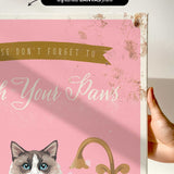 a hand holding a framed canvas print with a cat illustration and text.