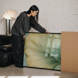 A woman in a gray sweater is leaning over a large framed print, examining it with interest.