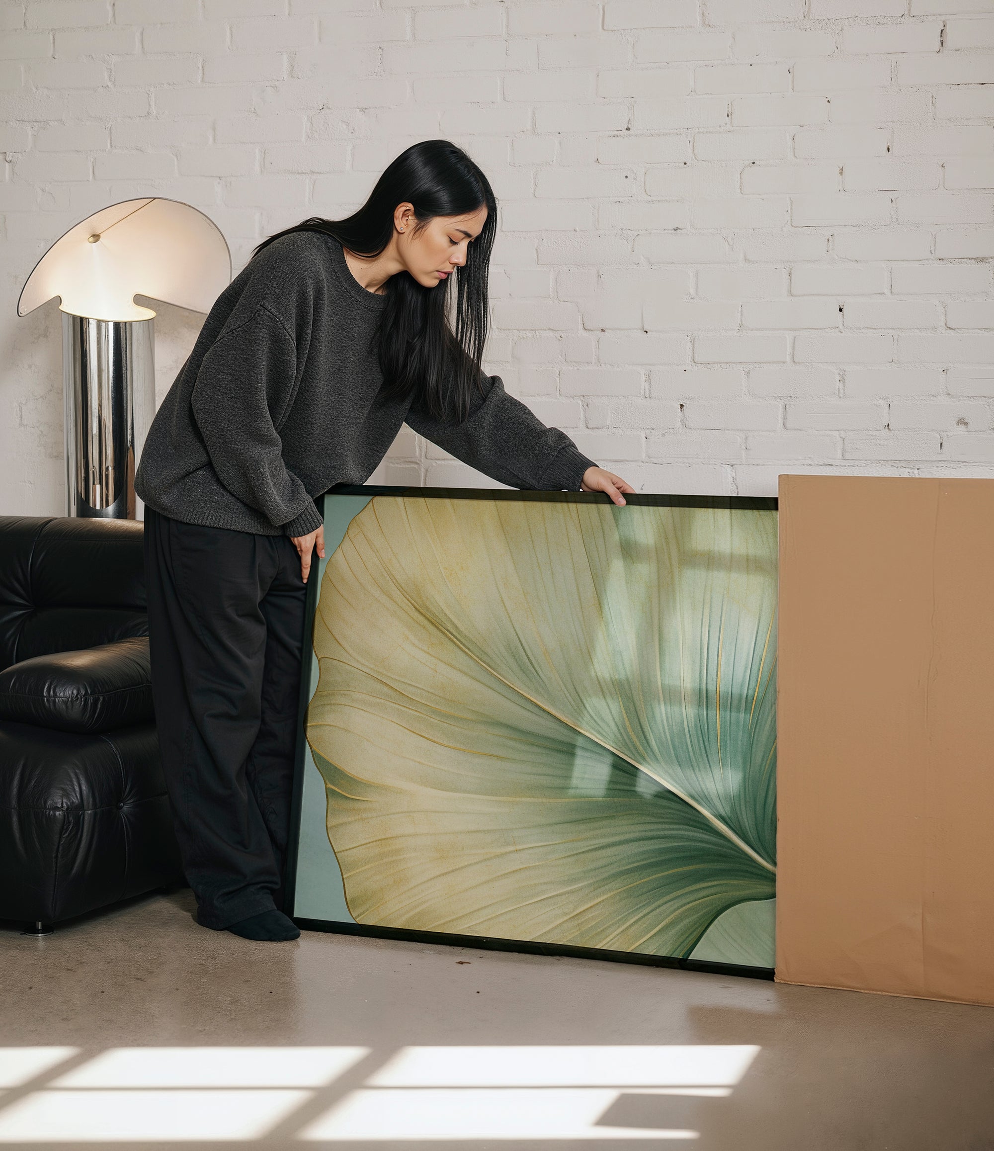 A woman in a gray sweater is leaning over a large framed print, examining it with interest.