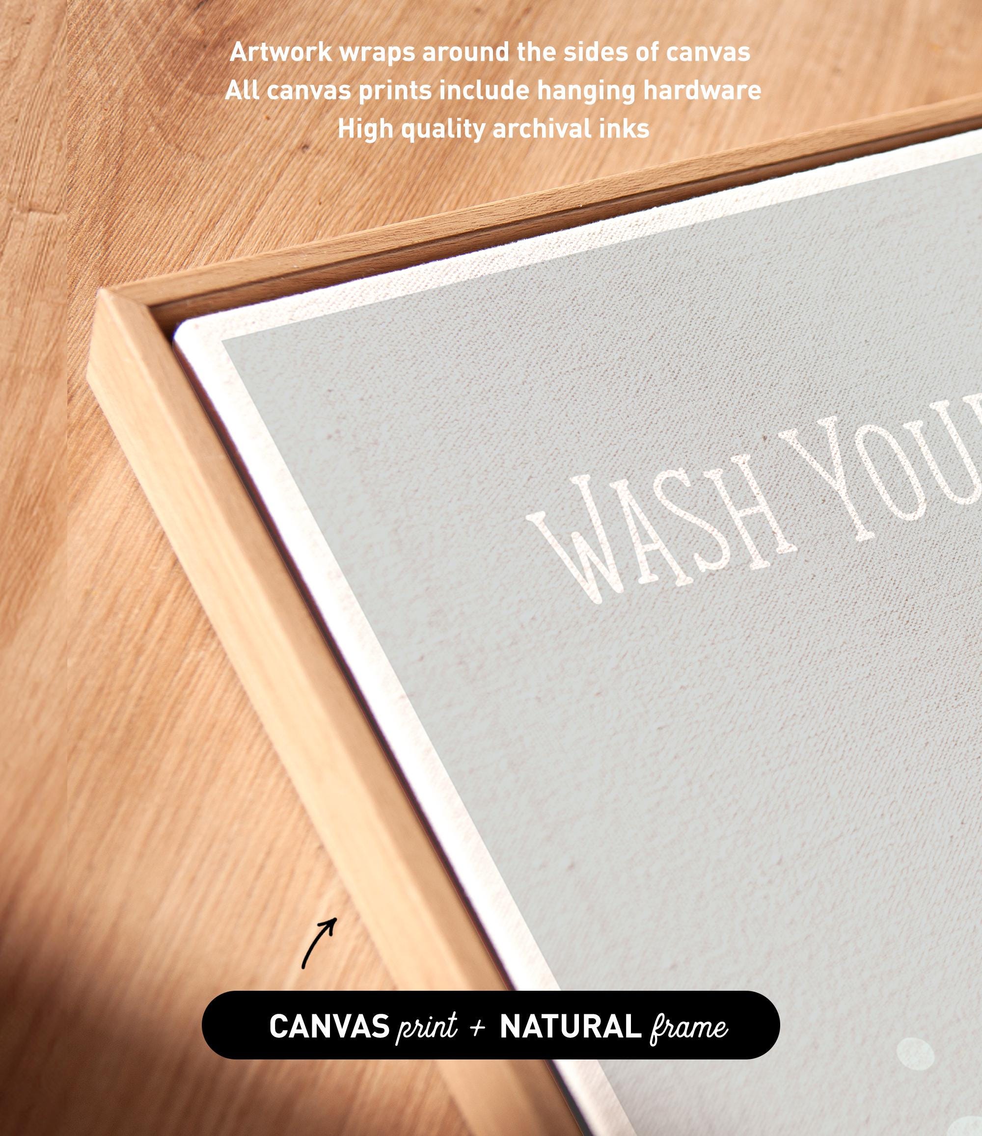 a close-up view of a canvas print with the phrase "WASH YOURS" prominently displayed on it. The print is framed in a natural frame, and the text indicates that the artwork wraps around the sides of the canvas, and all canvas prints include hanging hardware for high quality archival inks.