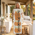 A woman stands on a porch holding a wooden sign with the word "PUMPKIN" written on it, accompanied by a golden retriever dog.