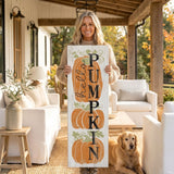 A woman stands on a porch holding a wooden sign with the word "PUMPKIN" written on it, accompanied by a golden retriever dog.