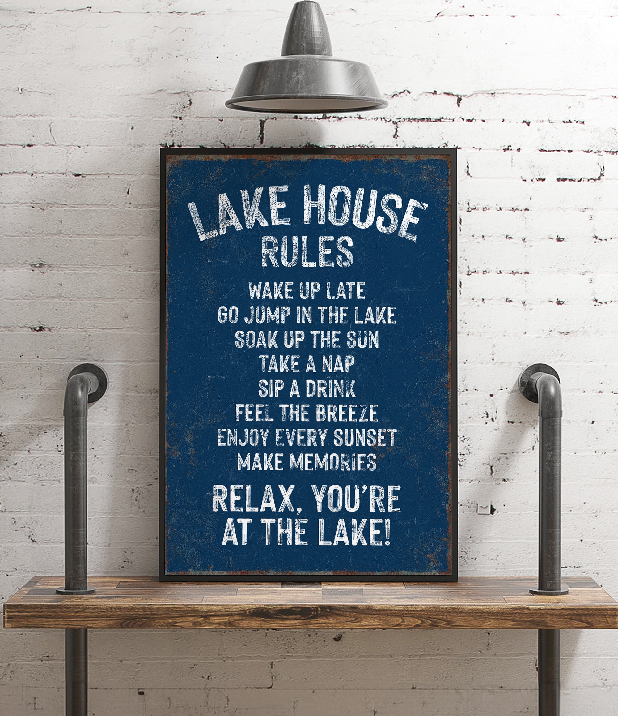 A blue sign with white text that reads "LAKESHOUSE RULES" is displayed on a wooden shelf against a white brick wall.