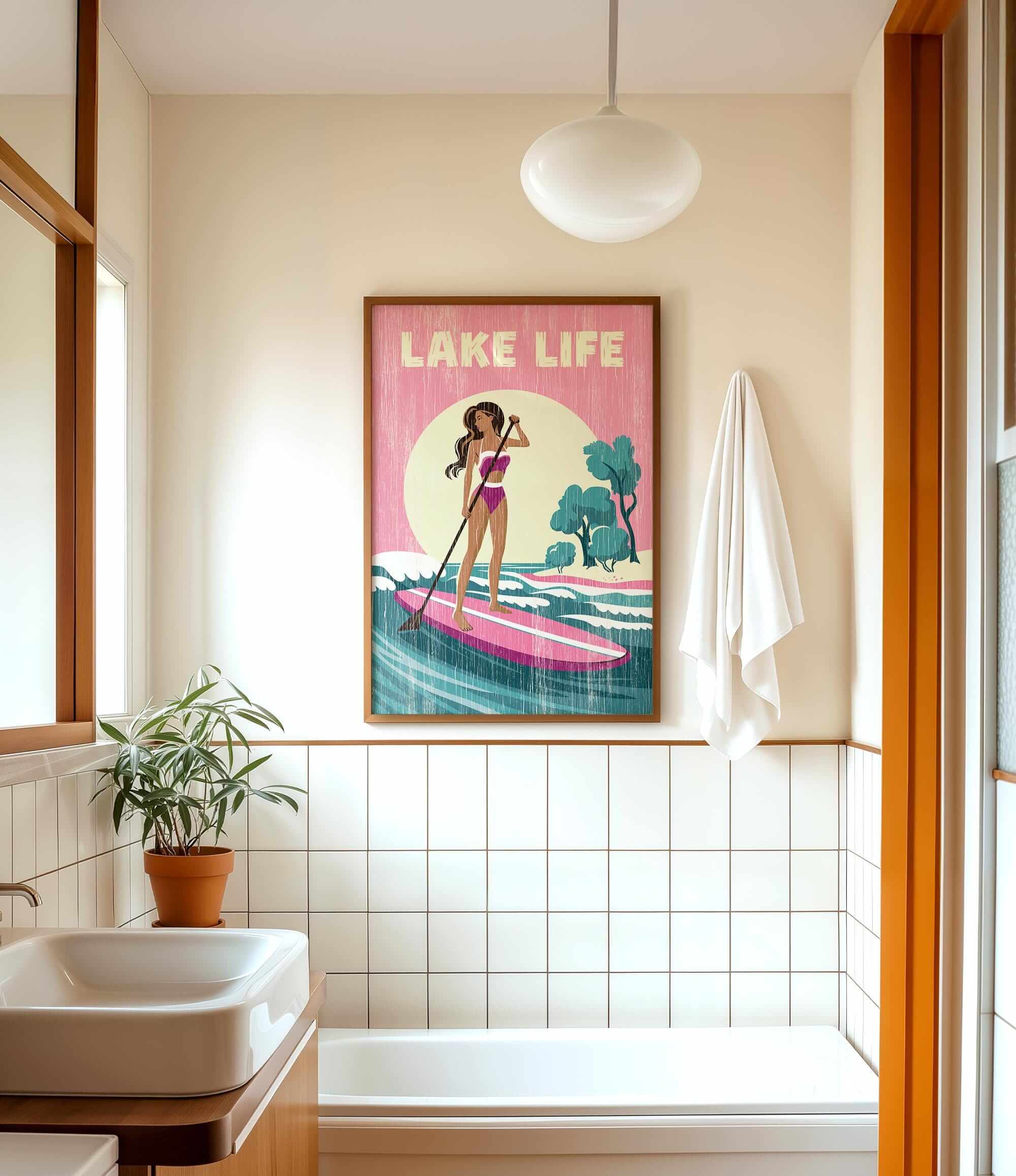 a bathroom with a framed poster of a woman paddleboarding, a potted plant, a sink, and a towel.