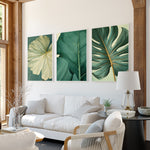 a modern living room with a white sofa, a black coffee table, and three framed prints of tropical leaves on the wall.