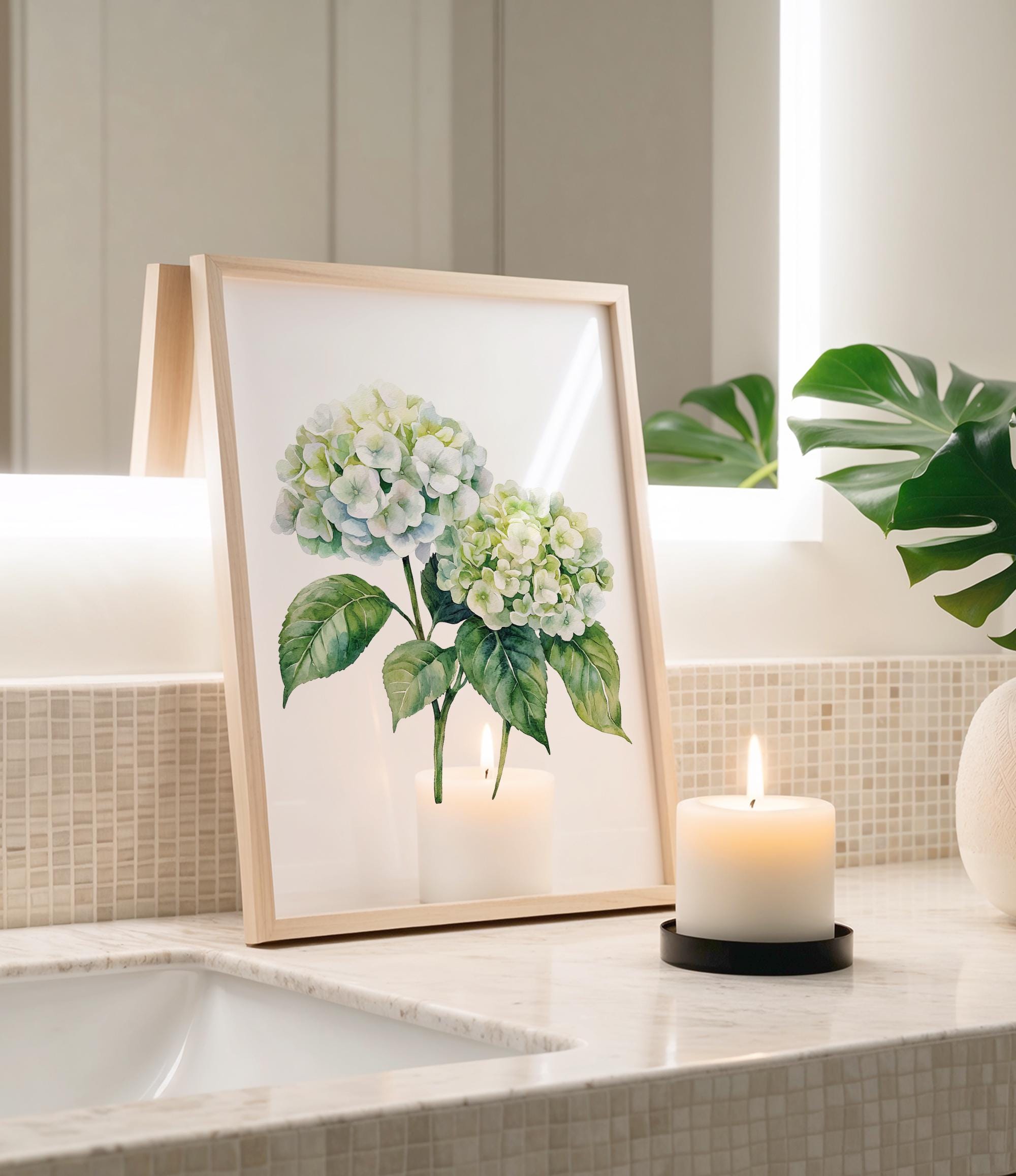 a framed painting of white hydrangeas and green leaves, placed on a bathroom counter next to a lit candle.
