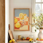 a kitchen counter with a framed painting of lemons and a glass of lemonade, a wooden cutting board, a vase of flowers, and various fruits and vegetables.