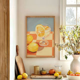 a kitchen counter with a framed painting of lemons and a glass of lemonade, a wooden cutting board, a vase of flowers, and various fruits and vegetables.