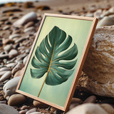 A framed image of a large green leaf is displayed on a rocky beach, with the natural elements of the beach and the leaf creating a serene and tranquil scene.