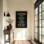 a hallway with a framed sign that reads "LAKESHORE RULES" hanging on the wall. The hallway has a wooden table with a vase of flowers, a rug, and a large window with a view of trees outside.