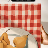 a hand holding a framed print of a red and white checkered tablecloth with a bowl containing three pears.