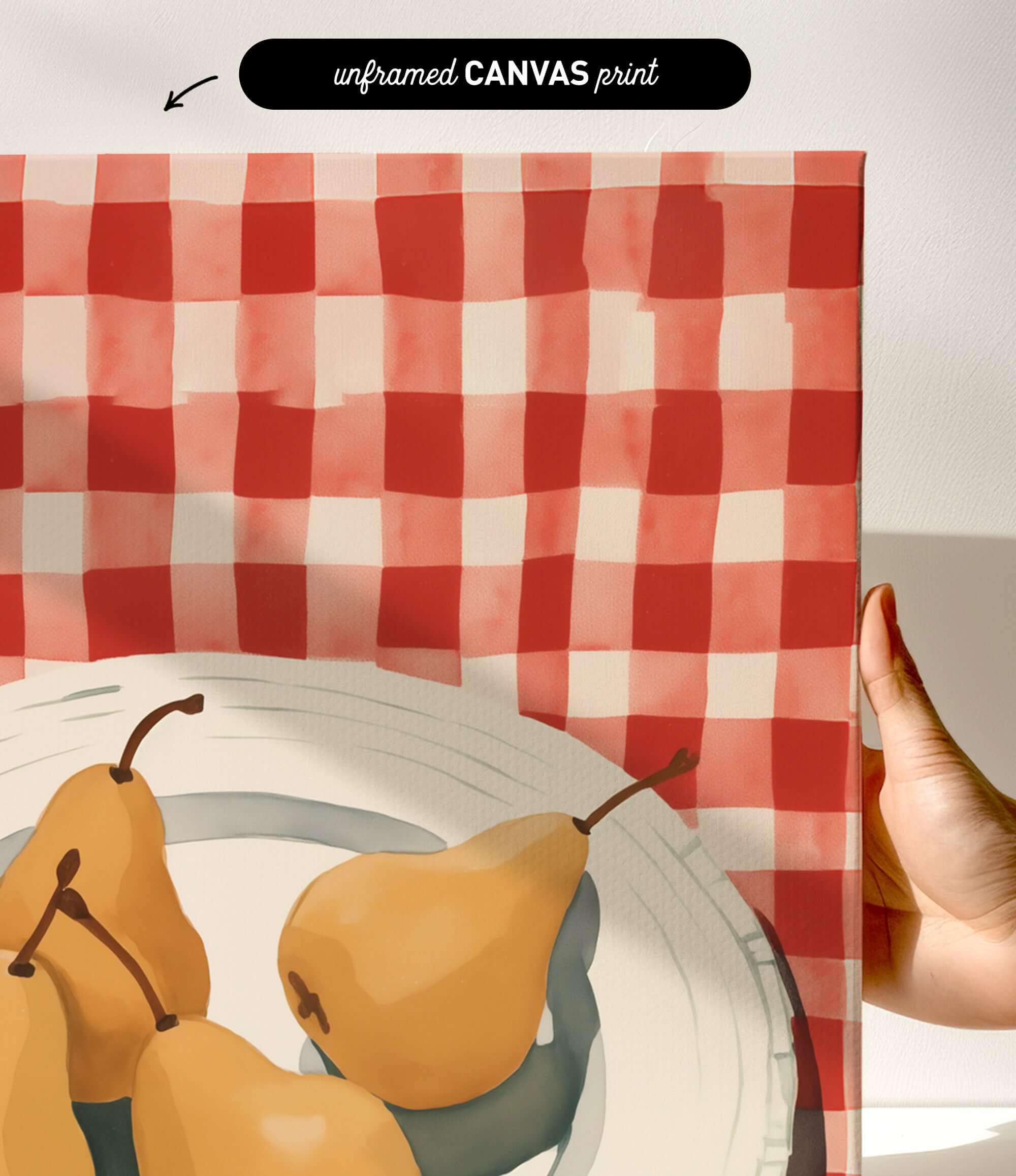 a hand holding a framed print of a red and white checkered tablecloth with a bowl containing three pears.