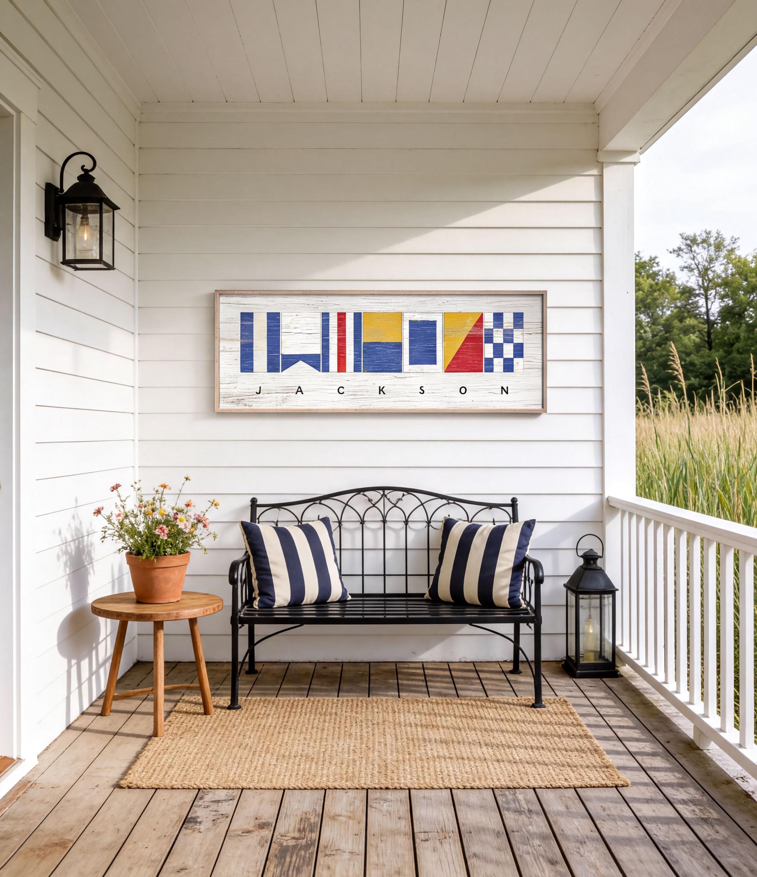 a porch with a bench, a small table, and a lantern, all set against a white wooden wall with a framed nautical flag artwork above it.