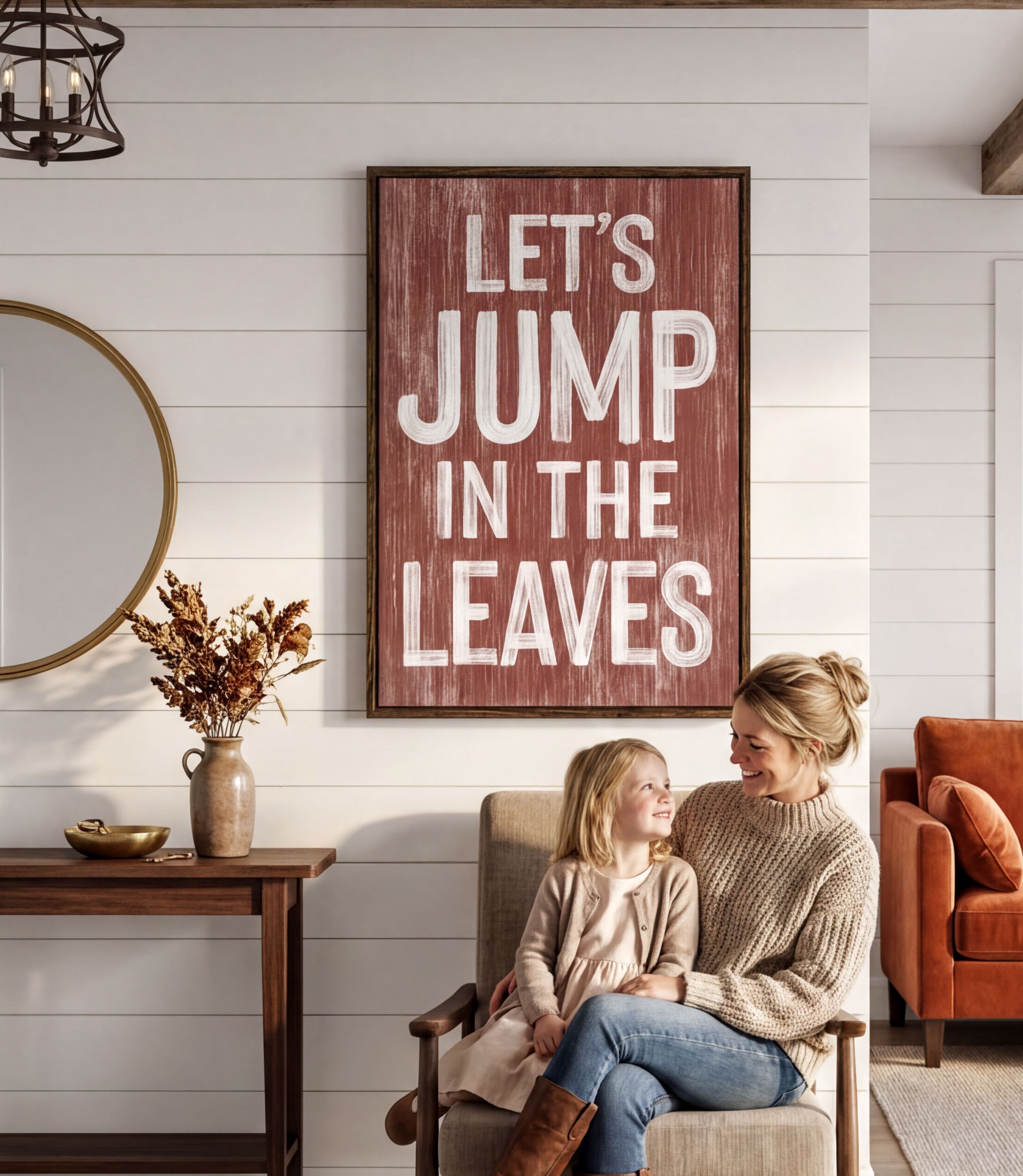 A woman and a young girl are sitting together in a cozy living room, with a large framed sign above them that reads "Let's JUMP IN THE LEAVES".