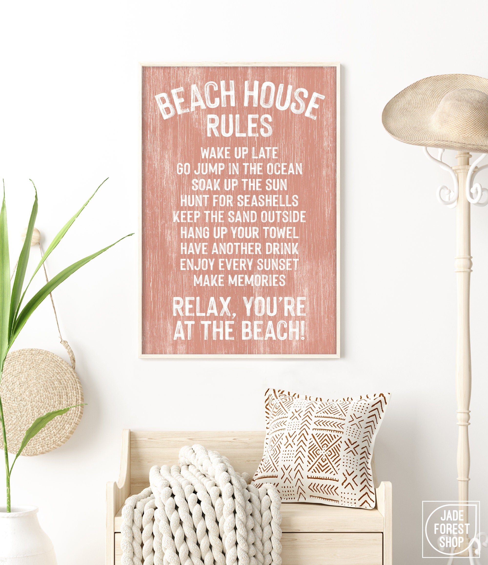 Bright room with coastal wall art, basket, pillows, straw hat, white walls, and a painted wood Coral Beach House Rules Sign.