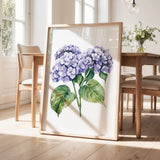 a framed painting of purple hydrangeas on a wooden table, with a vase of greenery and a wooden chair visible in the background.