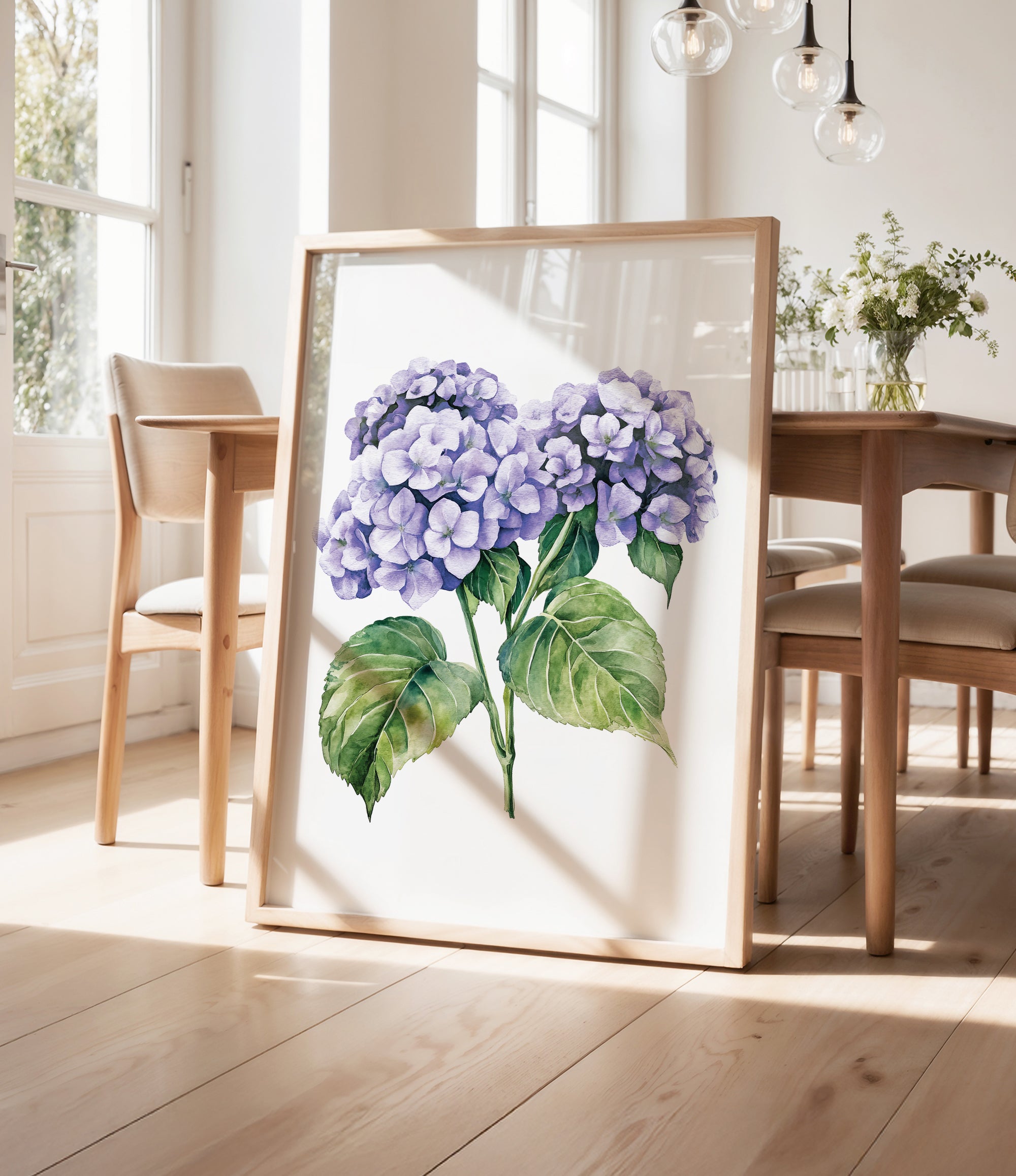 a framed painting of purple hydrangeas on a wooden table, with a vase of greenery and a wooden chair visible in the background.