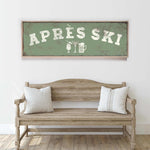 a wooden bench with two striped pillows, and above it is a framed sign with the text "APRÈS SKI" in white letters.