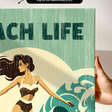 a hand holding a canvas print with a beach life theme, including a woman in a bathing suit and a wave.