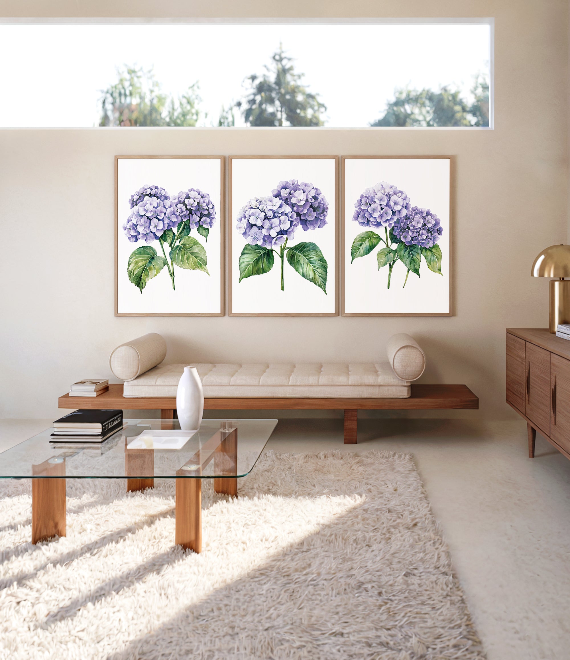 a modern living room with a glass coffee table, a wooden bench, and three framed watercolor paintings of purple hydrangeas hanging on the wall above the bench.