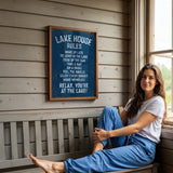 A woman is sitting on a bench in front of a sign that provides rules for the Lake House.